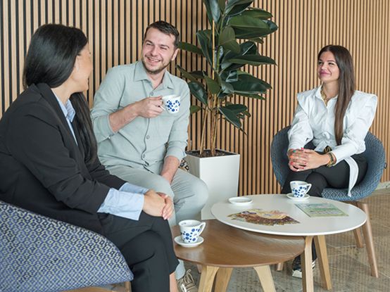 Dvije kolegice i kolega sjede nasmijani, piju kafu